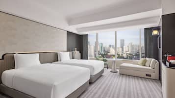 A modern hotel room with two beds, a sofa, and a city view.