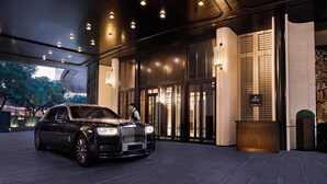 Un automóvil de lujo estacionado frente a la entrada de un hotel con diseño moderno y señalización iluminada.