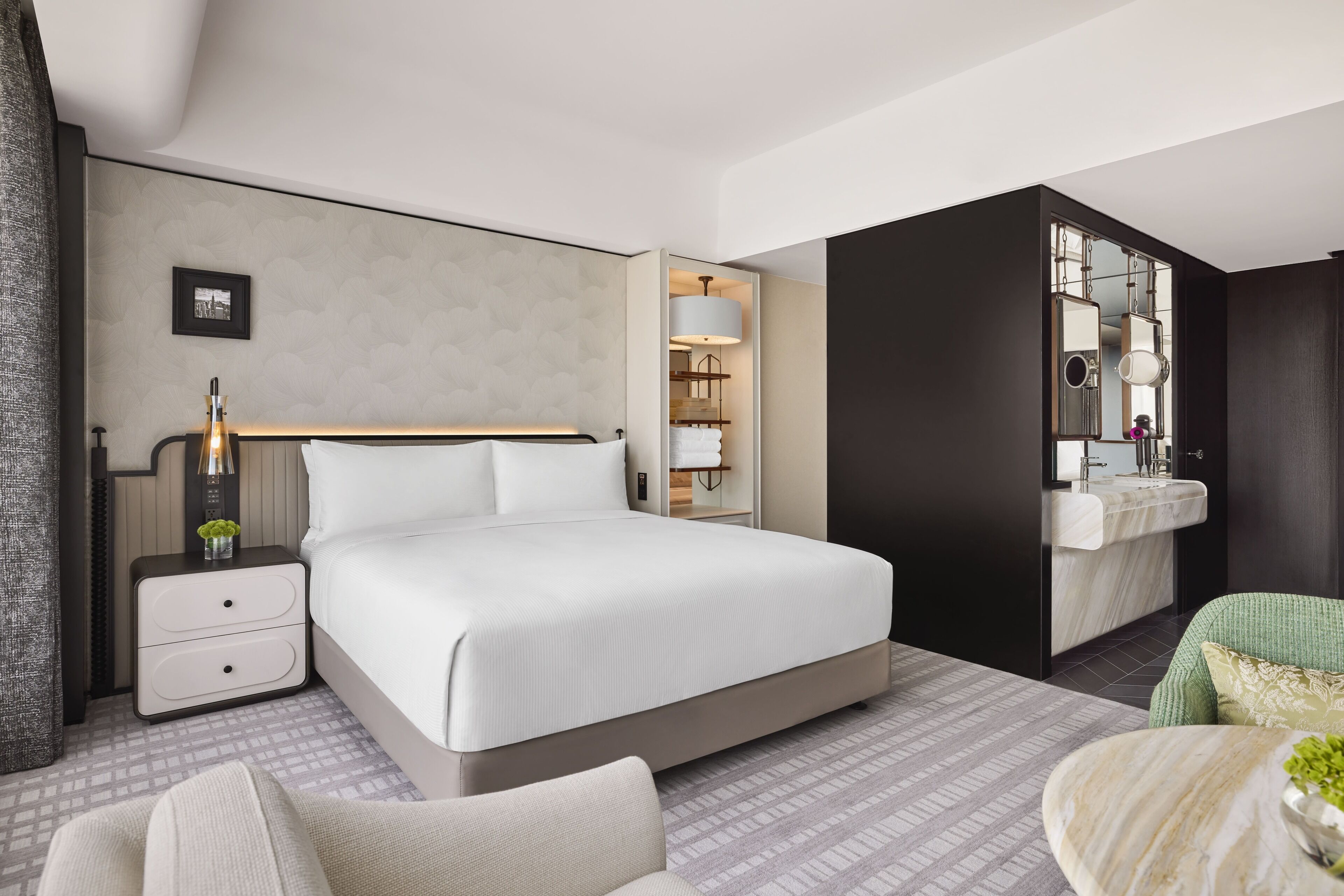 Camera d'albergo moderna con un letto grande, un comodino con lampada, un armadio e un bagno con specchio e lavandino.