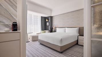 A modern hotel room with a large bed, a bedside table, a nightstand, a small table with a lamp, and a window with curtains.