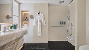 A modern bathroom with a marble vanity, a robe hanging on the wall, a shower area, and a small shelf with toiletries.