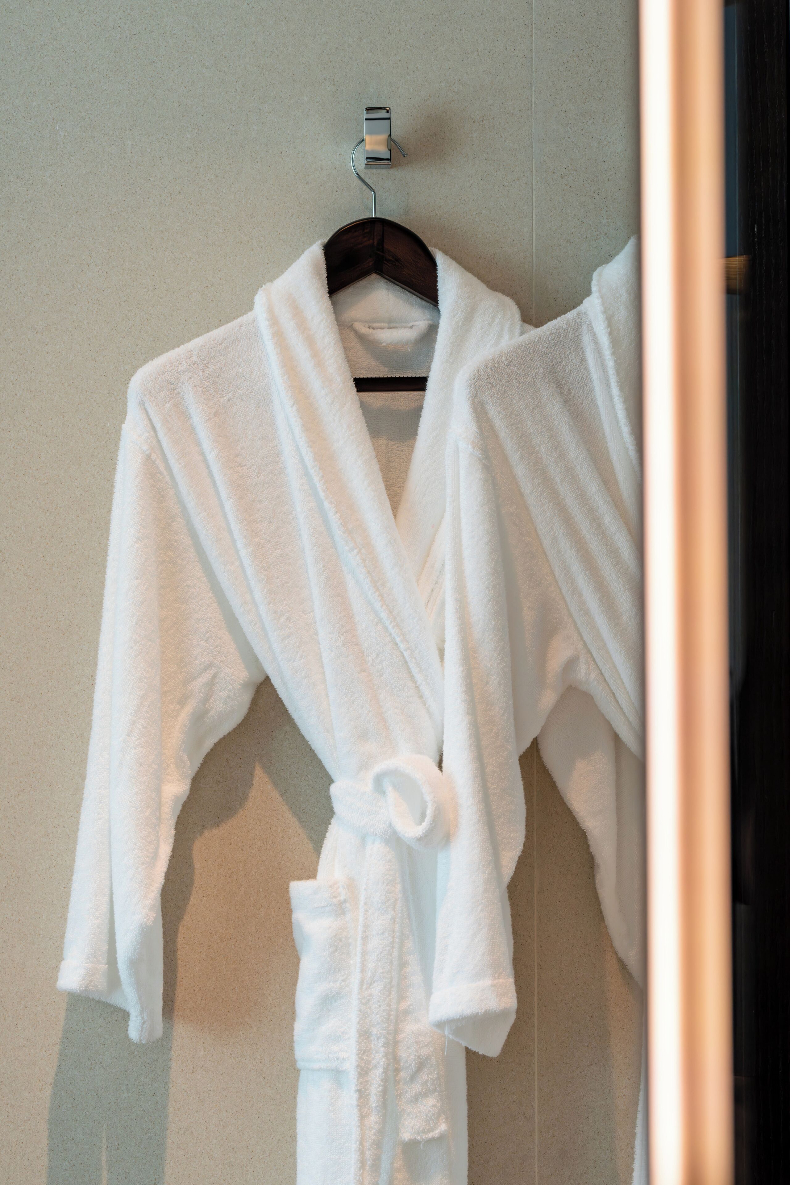 A white bathrobe hanging on a metal hook against a tiled wall.