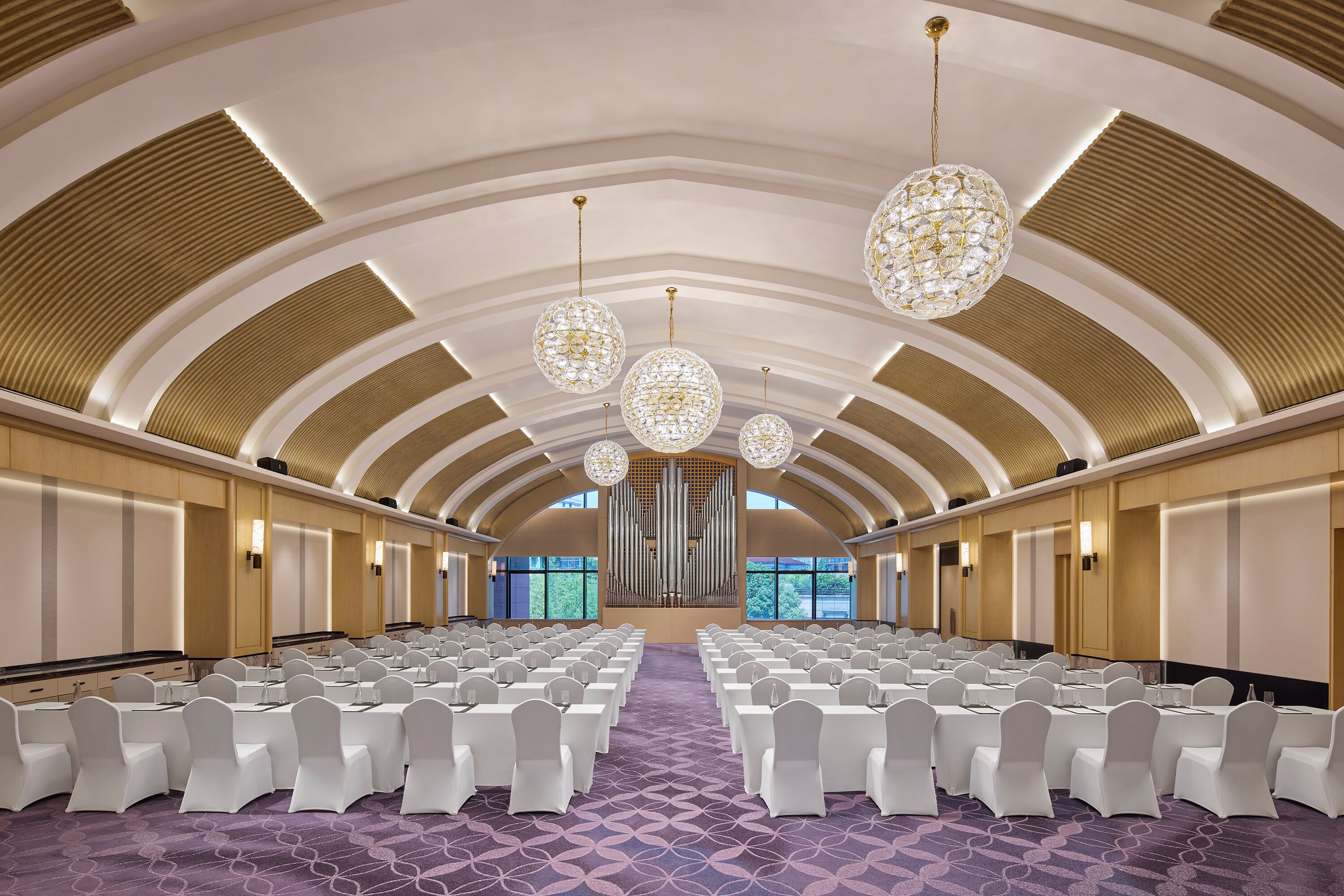 Une salle de conférence avec des rangées de chaises blanches, une scène centrale et un grand orgue.