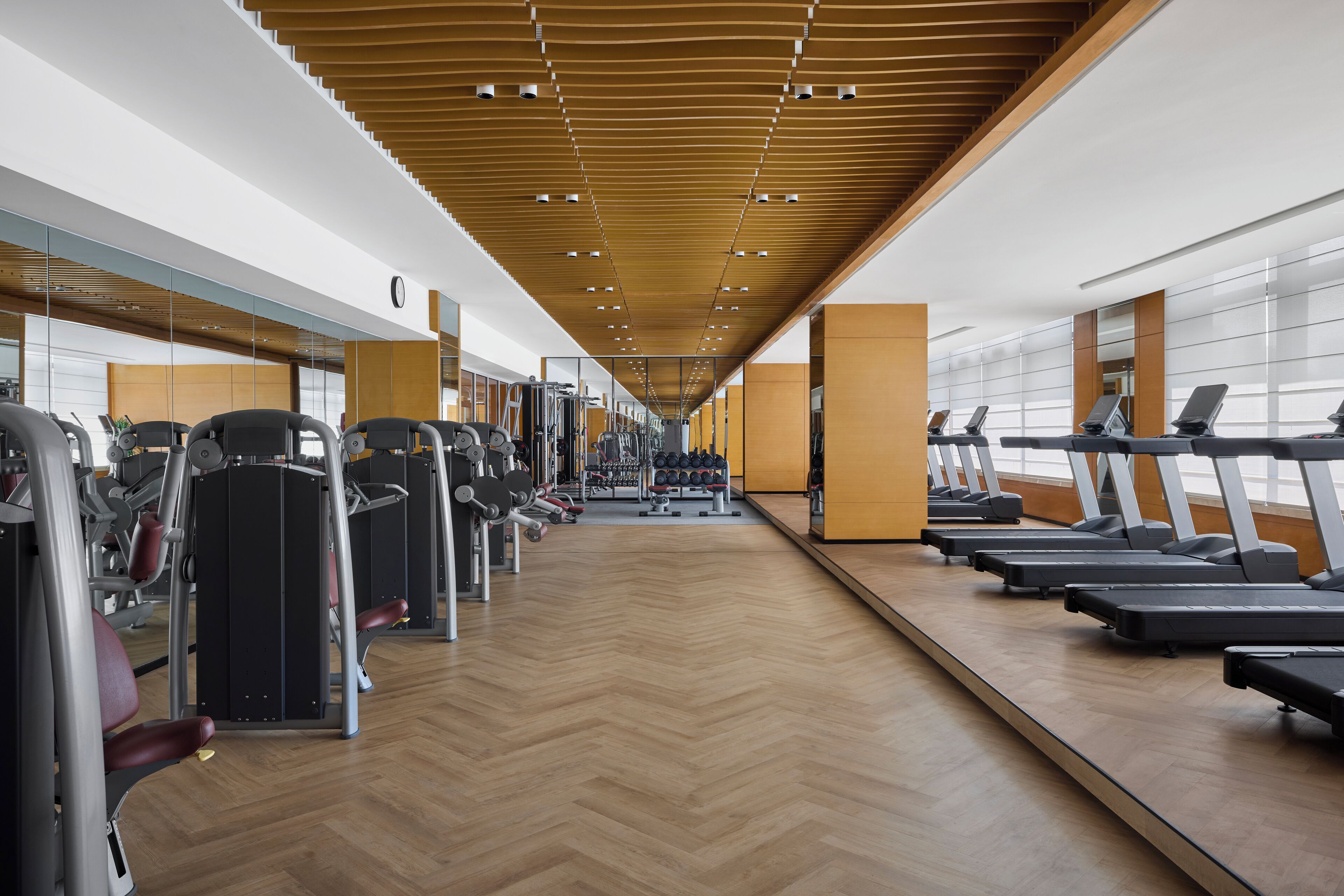 A gym with exercise equipment, mirrored walls, and a wooden floor.