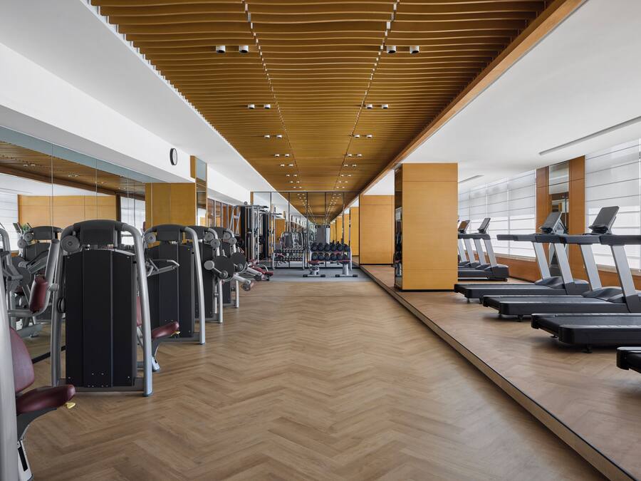 A gym with exercise equipment, mirrored walls, and a wooden floor.