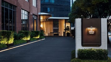 Une entrée d’hôtel moderne, avec un chemin bien éclairé, un comptoir d’accueil et une enseigne indiquant la marque Hilton.