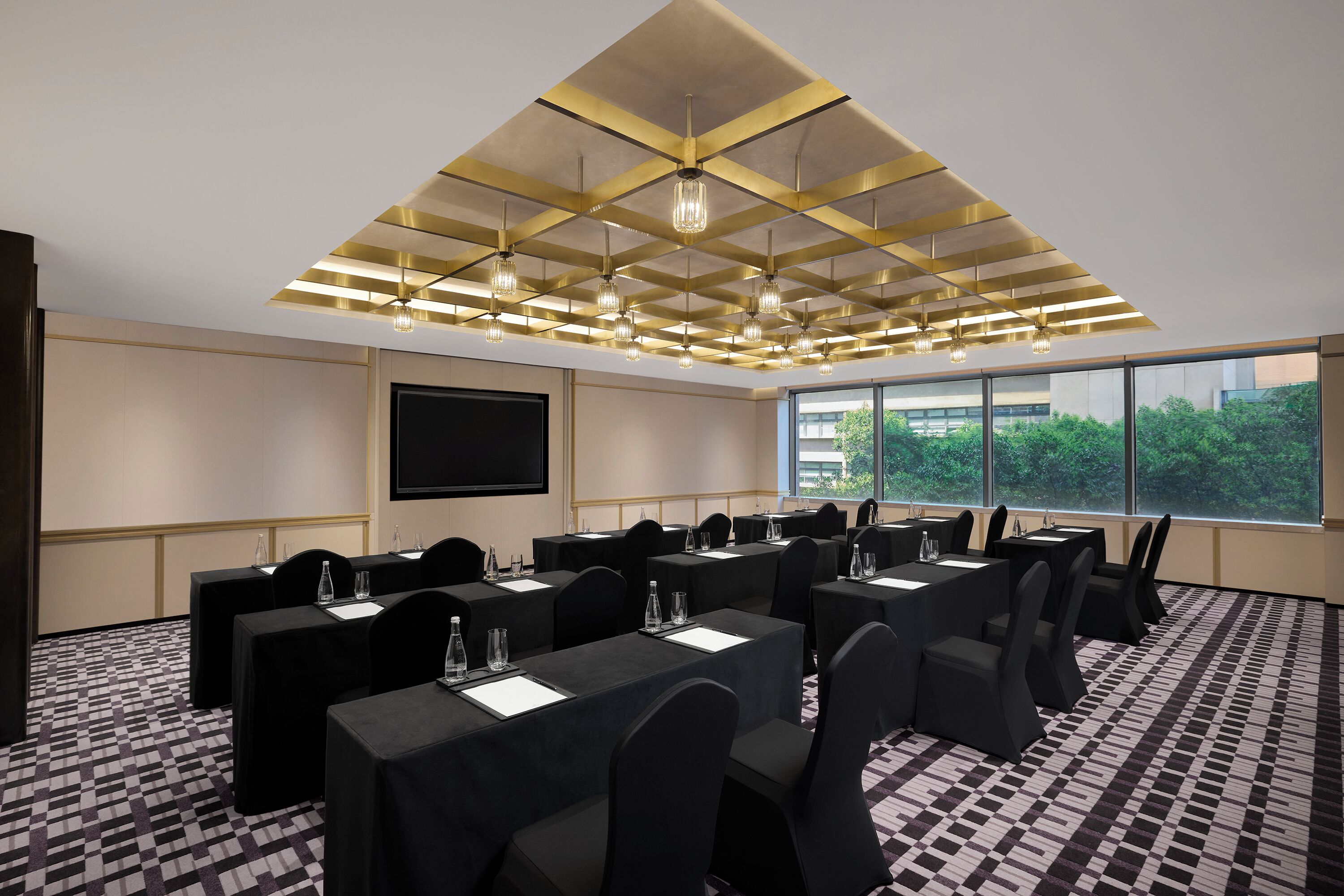 Ein Konferenzraum mit Schachbrettmuster-Boden, Tischen mit Stühlen, einer großen Leinwand und einer Decke mit geometrischem Muster.
