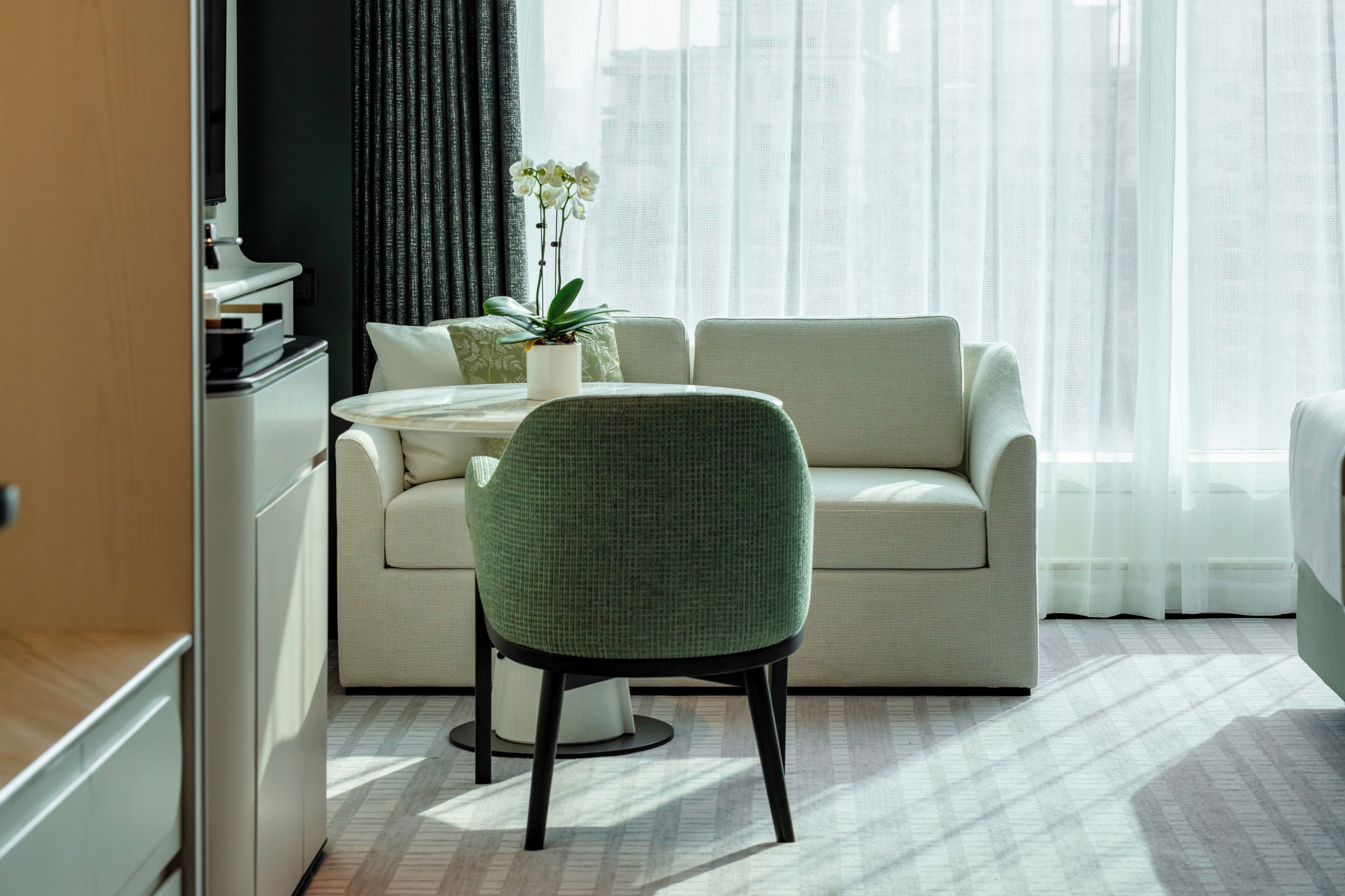 Een moderne hotelkamer met een bank, een groene fauteuil, een kleine ronde tafel en een potplant.