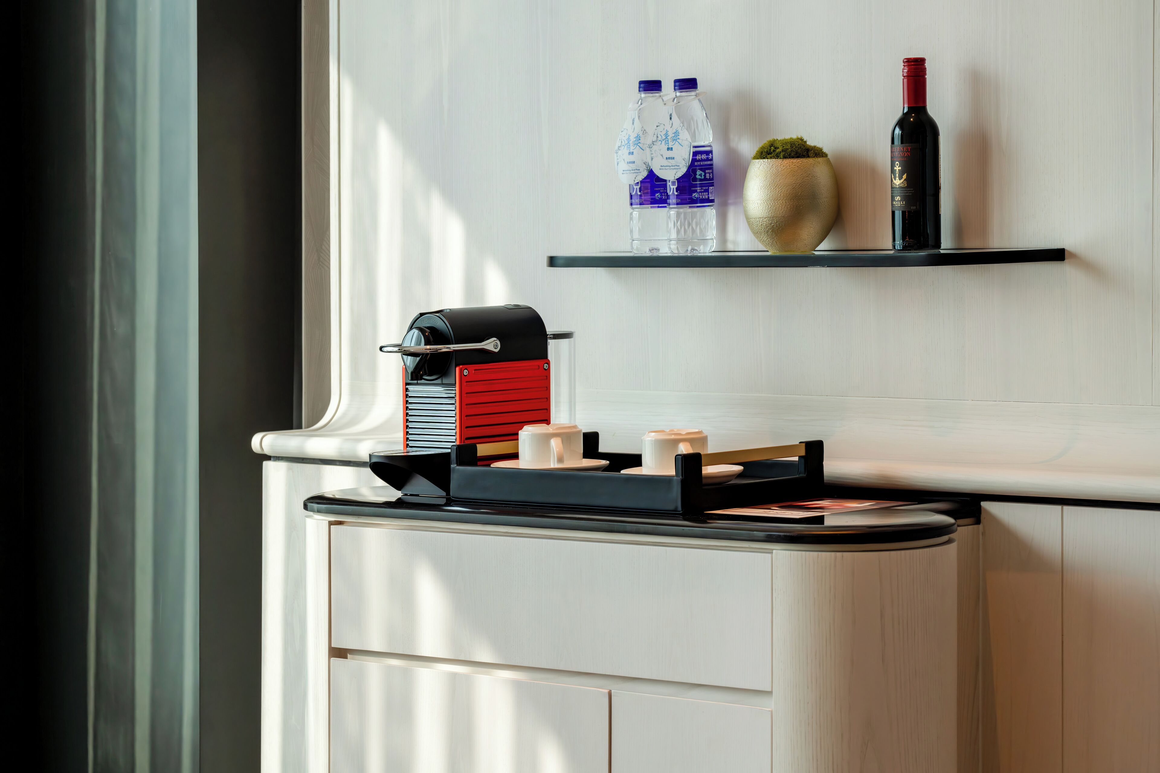 A kitchen counter with a coffee machine, a water dispenser, and a wine bottle on a shelf.