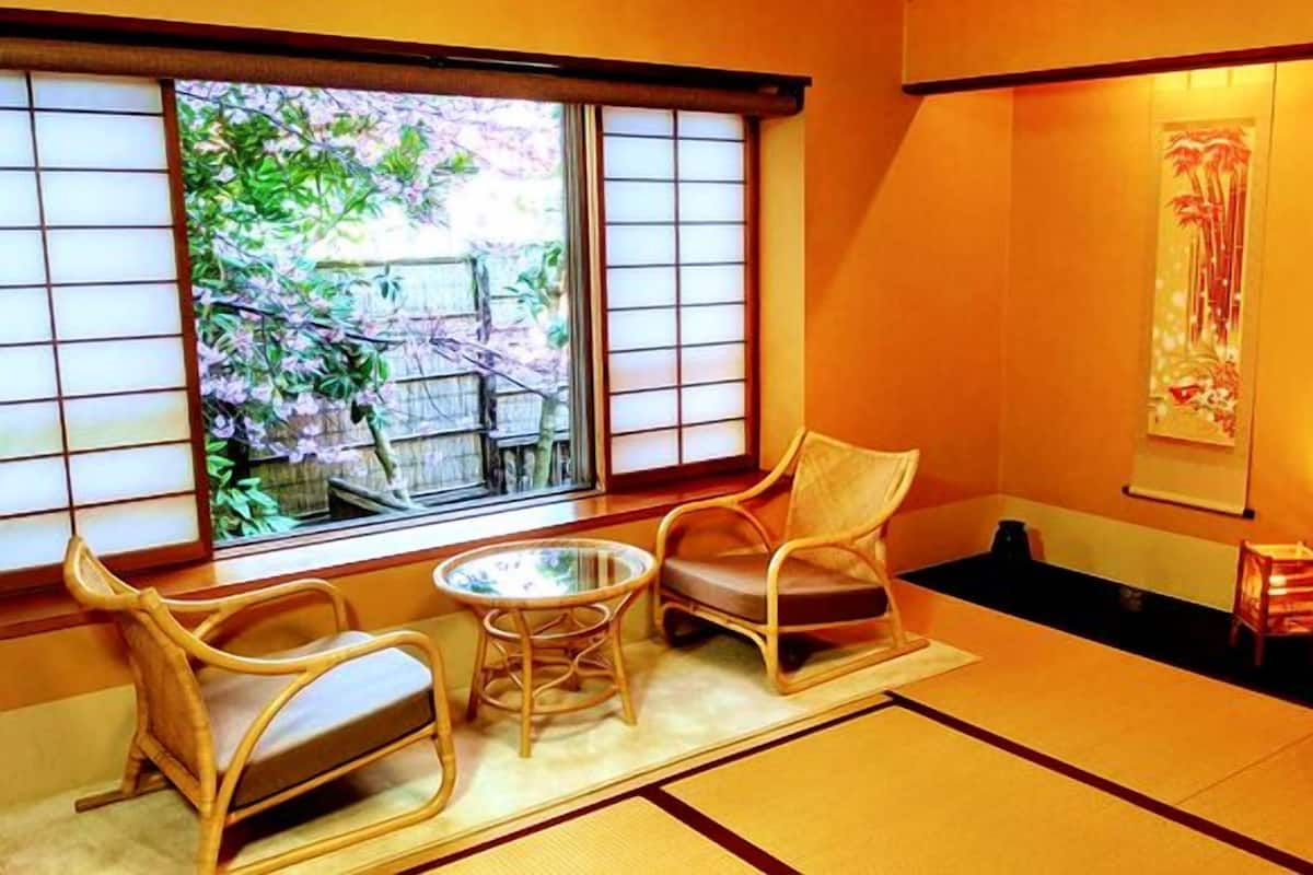 Une pièce de style japonais traditionnel, avec un sol recouvert de tatamis, une table basse, deux chaises et une porte coulissante.