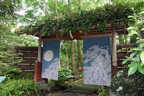 A traditional Japanese garden with a wooden pergola, bamboo fence, and hanging scrolls. - Hanafubuki (Ito)