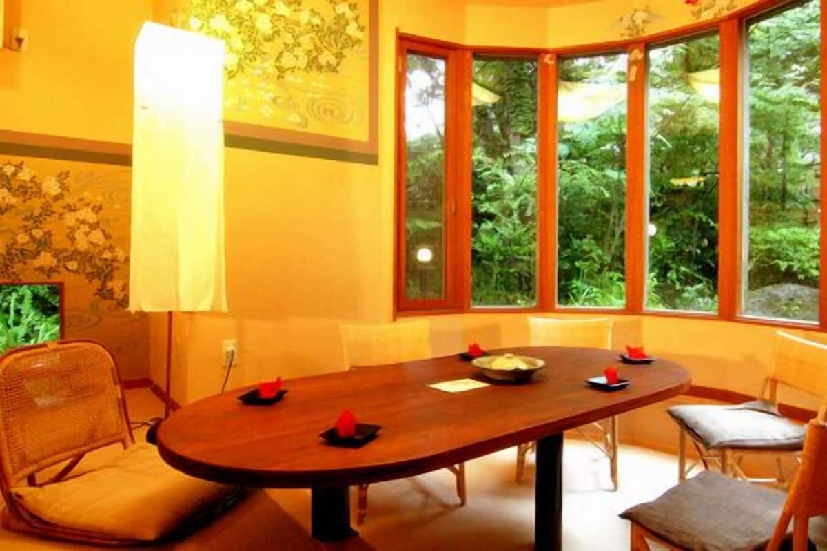 Un espace repas avec une table en bois, des chaises et une vue sur la verdure grâce à de grandes fenêtres.