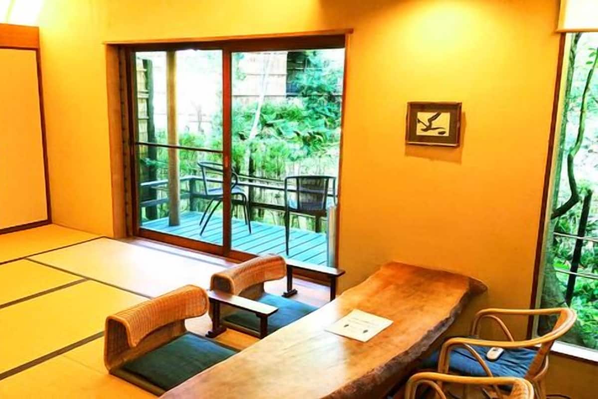 Une pièce de style japonais traditionnel, avec un sol recouvert de tatamis, une table basse et une porte coulissante donnant sur une terrasse extérieure.