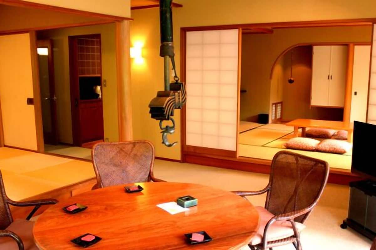 Une pièce de style japonais traditionnel, avec un sol recouvert de tatamis, une table basse entourée de chaises, un téléviseur et des portes coulissantes.