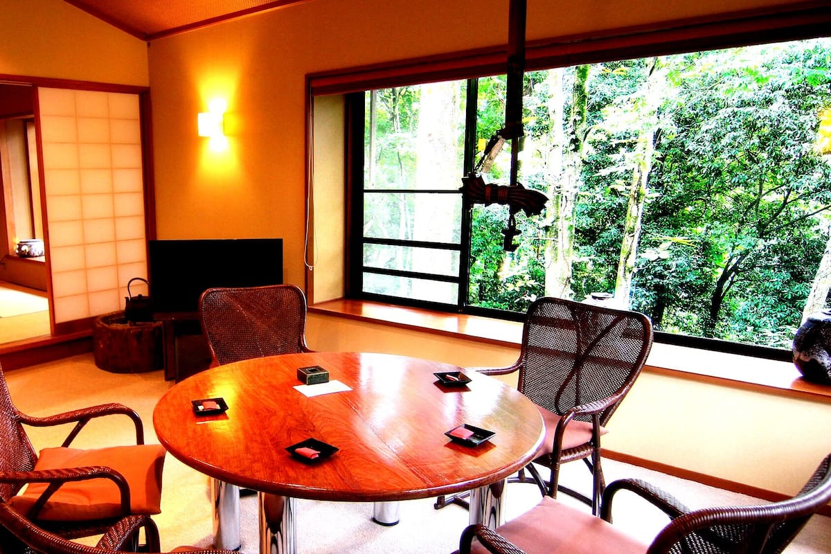 Une pièce de style japonais traditionnel, avec un sol recouvert de tatamis, une table ronde en bois et de petites chaises en bois.