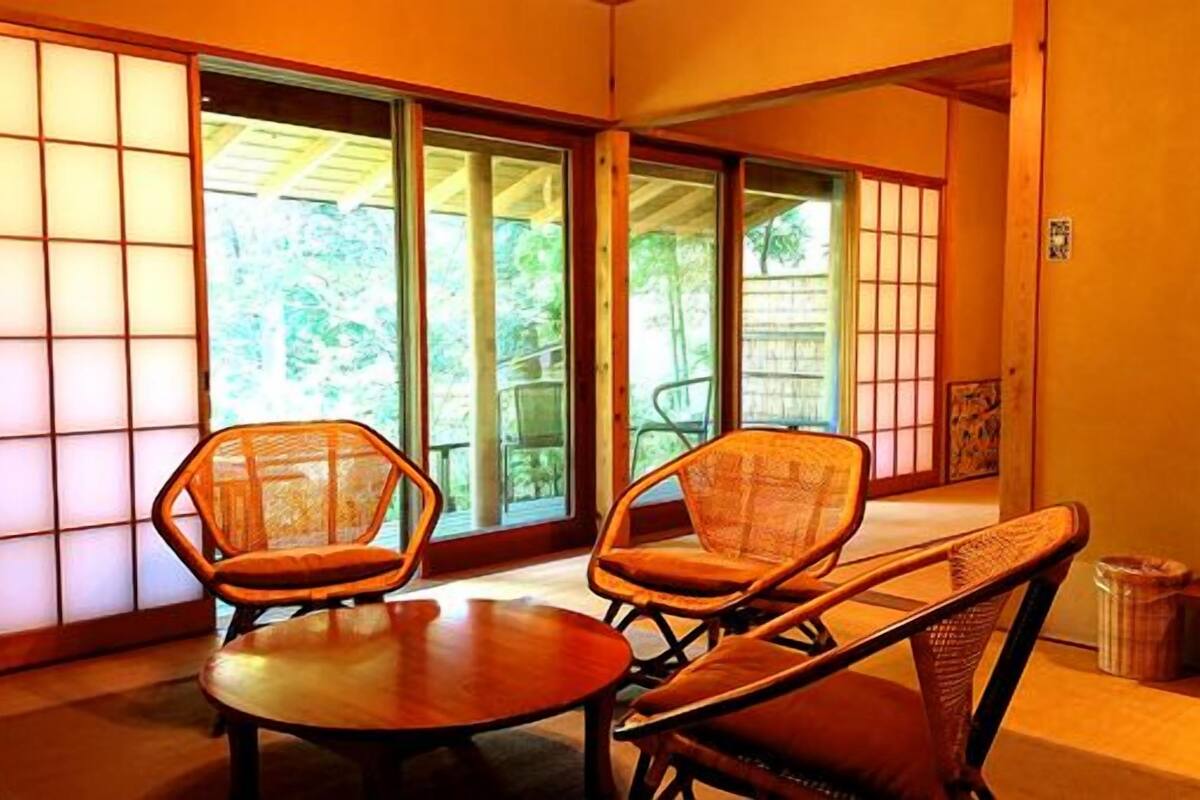 Une pièce de style japonais traditionnel, avec un sol recouvert de tatamis, des portes coulissantes et deux chaises en bois.