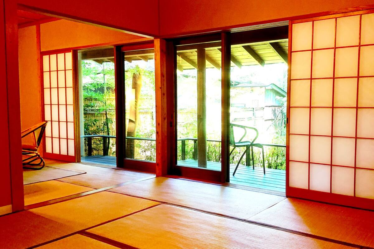 Une pièce de style japonais traditionnel, avec un sol recouvert de tatamis, des portes coulissantes et une vue sur la verdure environnante.