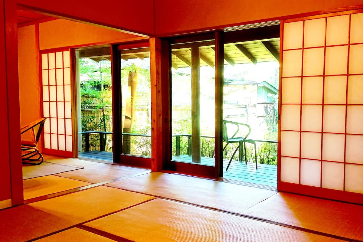 Une pièce de style japonais traditionnel, avec un sol recouvert de tatamis, des portes coulissantes et une vue sur la verdure environnante.