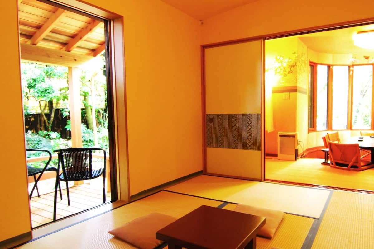 Une pièce de style japonais traditionnel, avec un sol recouvert de tatamis, une porte coulissante donnant sur un espace extérieur et une table à manger avec des chaises.