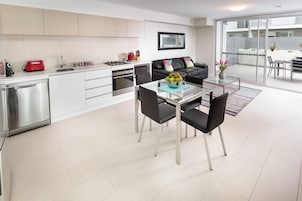 A modern kitchen with white cabinets, a red toaster, and a dining area with a glass table and black chairs.