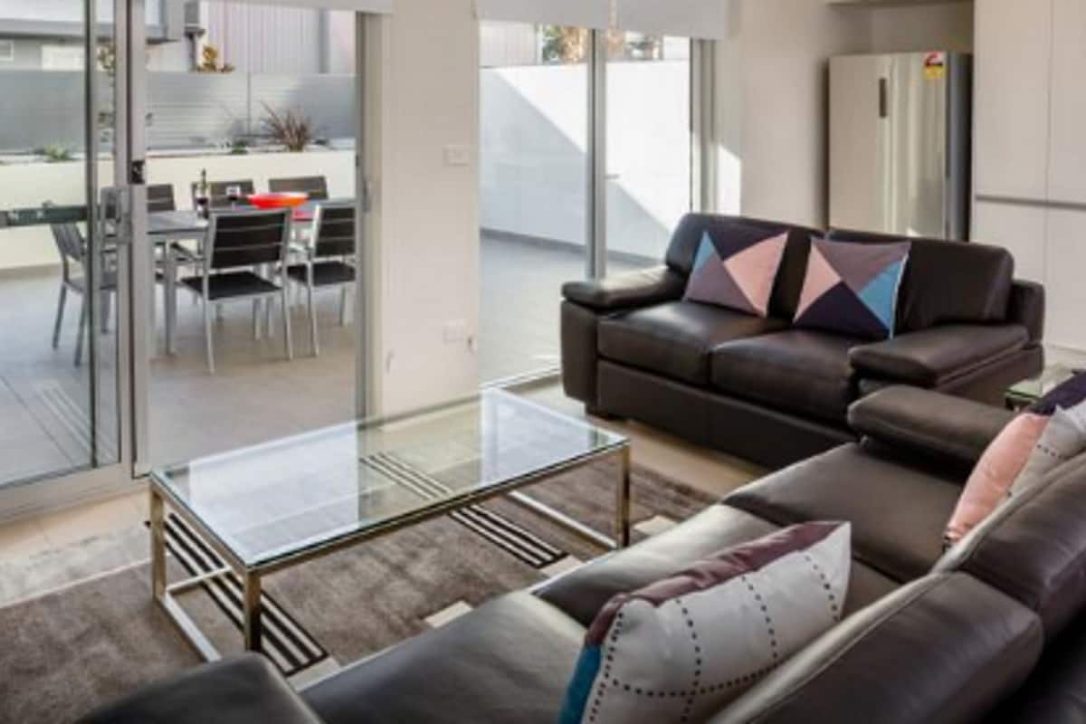 A modern living room with a glass coffee table, leather sofa, and a dining area with a table and chairs.