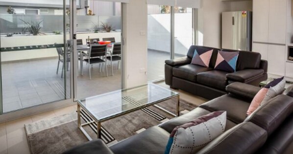 A modern living room with a glass coffee table, leather sofa, and a dining area with a table and chairs.