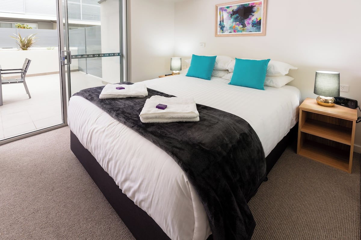 A hotel room with a large bed, two bedside tables with lamps, a glass door leading to a balcony, and a painting on the wall.