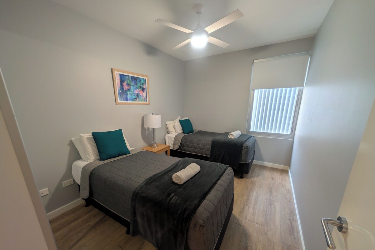 A bedroom with two beds, a ceiling fan, a window with blinds, and a painting on the wall.