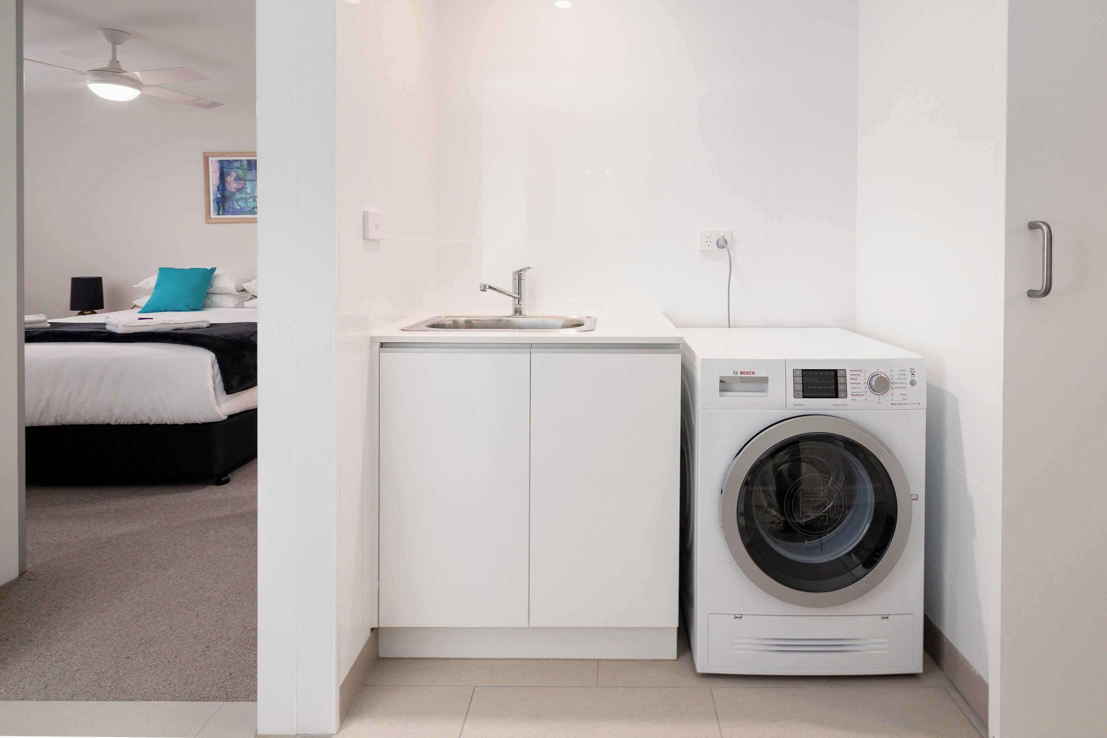 Una habitación de hotel compacta con una cama, una kitchenette pequeña con un lavamanos y una lavadora de carga frontal.