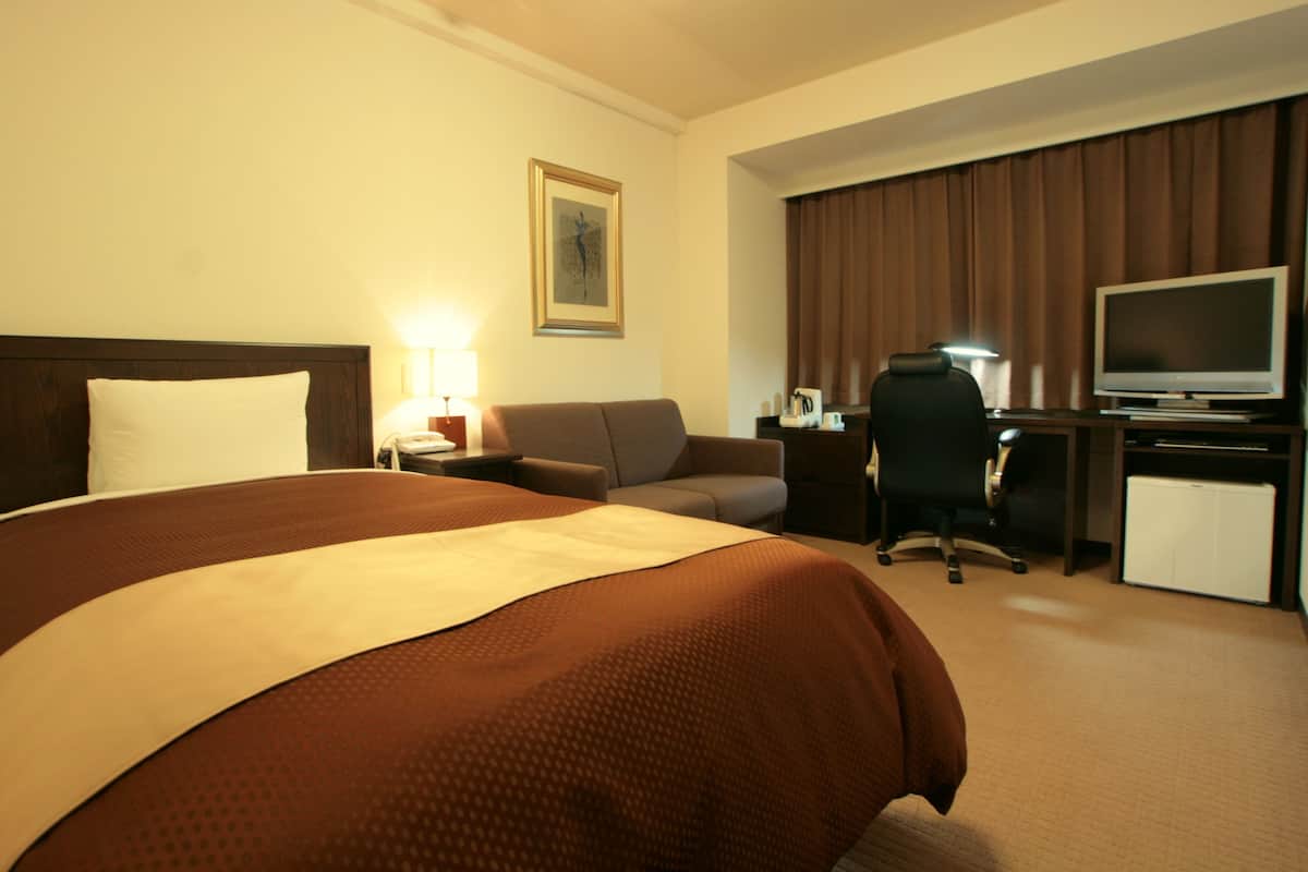 A hotel room with a large bed, a desk with a computer, a television, and a couch.