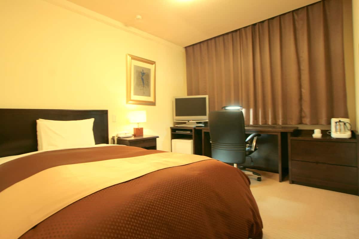 A hotel room with a large bed, a desk with a computer, a chair, and a coffee maker.