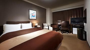 A hotel room with a large bed, a desk with a chair, a television, and a small refrigerator.