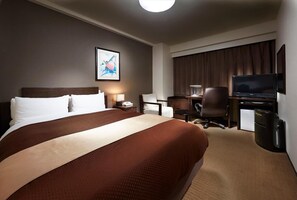 Une chambre d’hôtel avec un grand lit, un bureau avec une chaise, une télévision et un petit réfrigérateur.