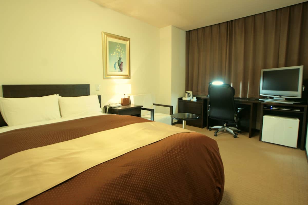 A hotel room with a large bed, a desk with a computer, a television, and a small refrigerator.