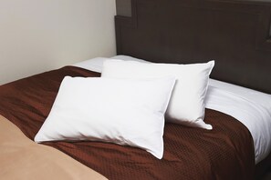 Un lit bien fait, avec deux oreillers blancs et une couverture marron.