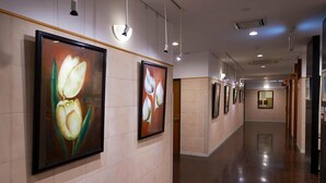 Un pasillo con cuadros de motivos florales en las paredes, iluminación empotrada y suelo pulido.