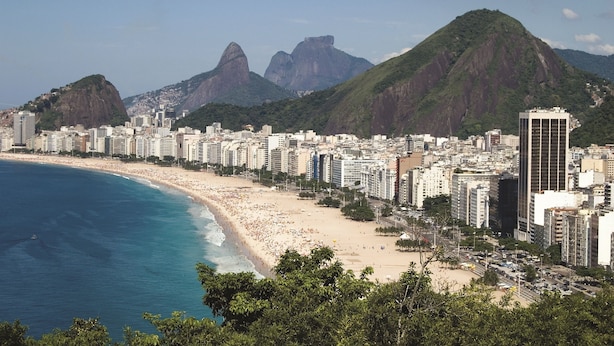 Un paysage urbain côtier avec une plage, des immeubles de grande hauteur et des montagnes imposantes en arrière-plan.