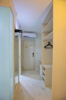 A hallway with a white door, a white wardrobe, and a white shelf unit with a black hanger.
