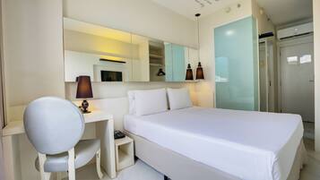 A hotel room with a bed, a desk, a chair, a mirror, and a wardrobe.