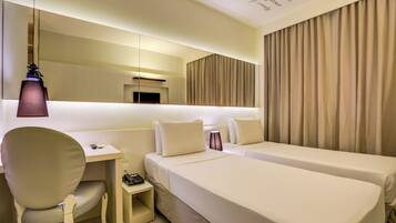 A hotel room with a desk, two beds, a chair, a lamp, and a curtain.