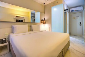 Una habitación de hotel con una cama grande, una mesita de noche con un teléfono, un espejo y una puerta que da a otra habitación.