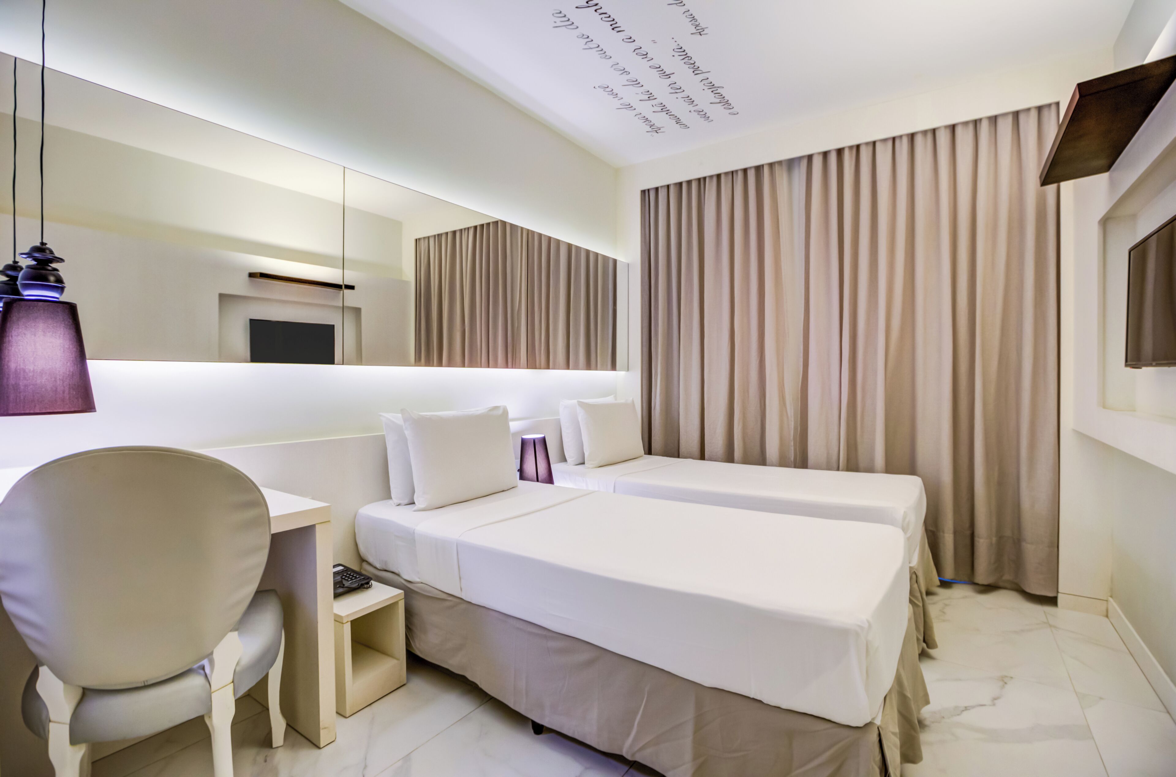 Une chambre d’hôtel avec deux lits, un bureau, une chaise, une télévision et une grande fenêtre avec des rideaux.