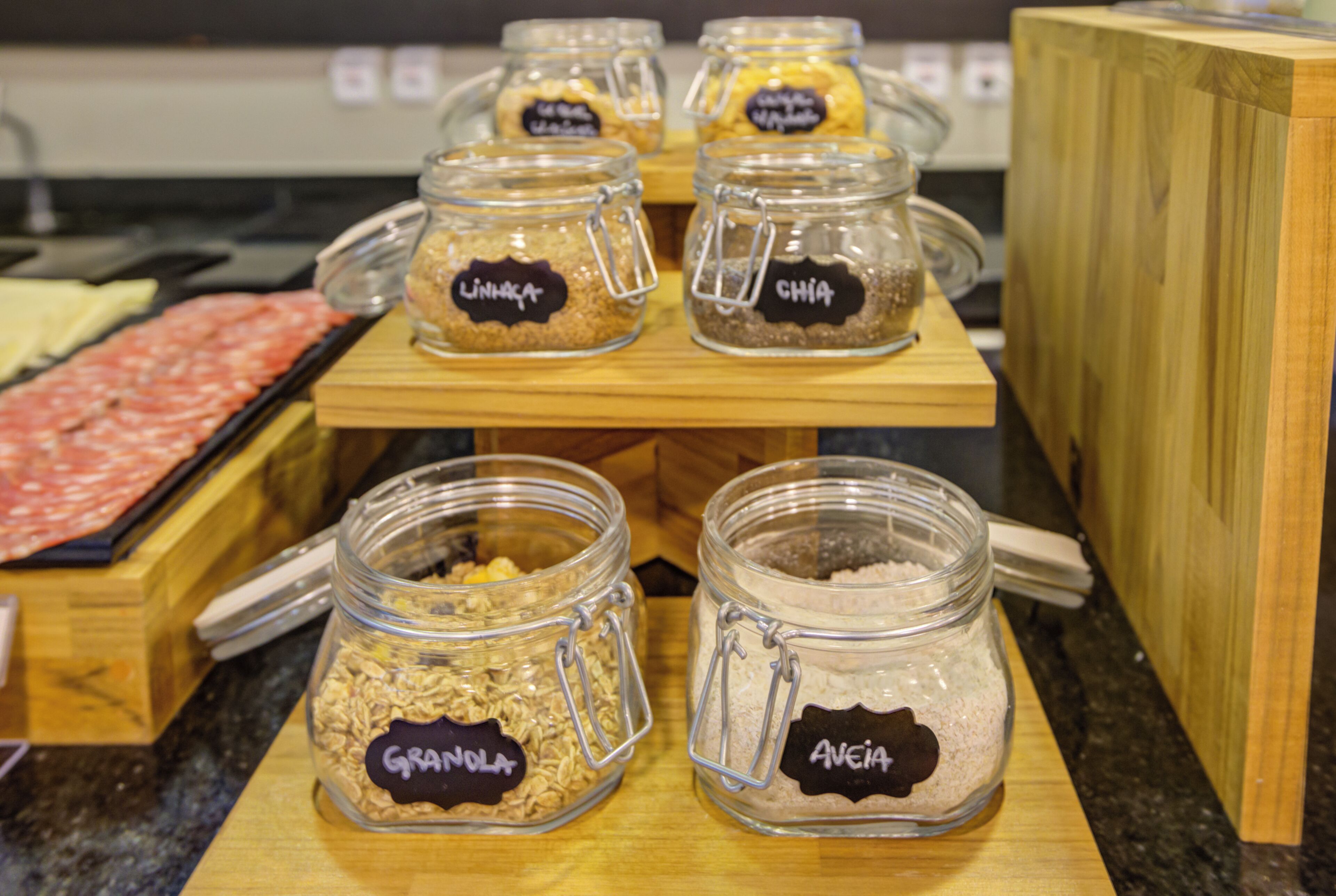 A display of food items in glass jars with labels, arranged on a wooden stand.