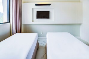 A hotel room with two single beds, a built-in TV, and a window with curtains.
