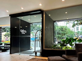 A hotel entrance with a glass door, a sign reading 'aera HOTEL', and a view of the street outside.