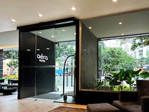 Entrada de hotel con puerta de vidrio, un letrero que dice 'aera HOTEL' y vista de la calle.