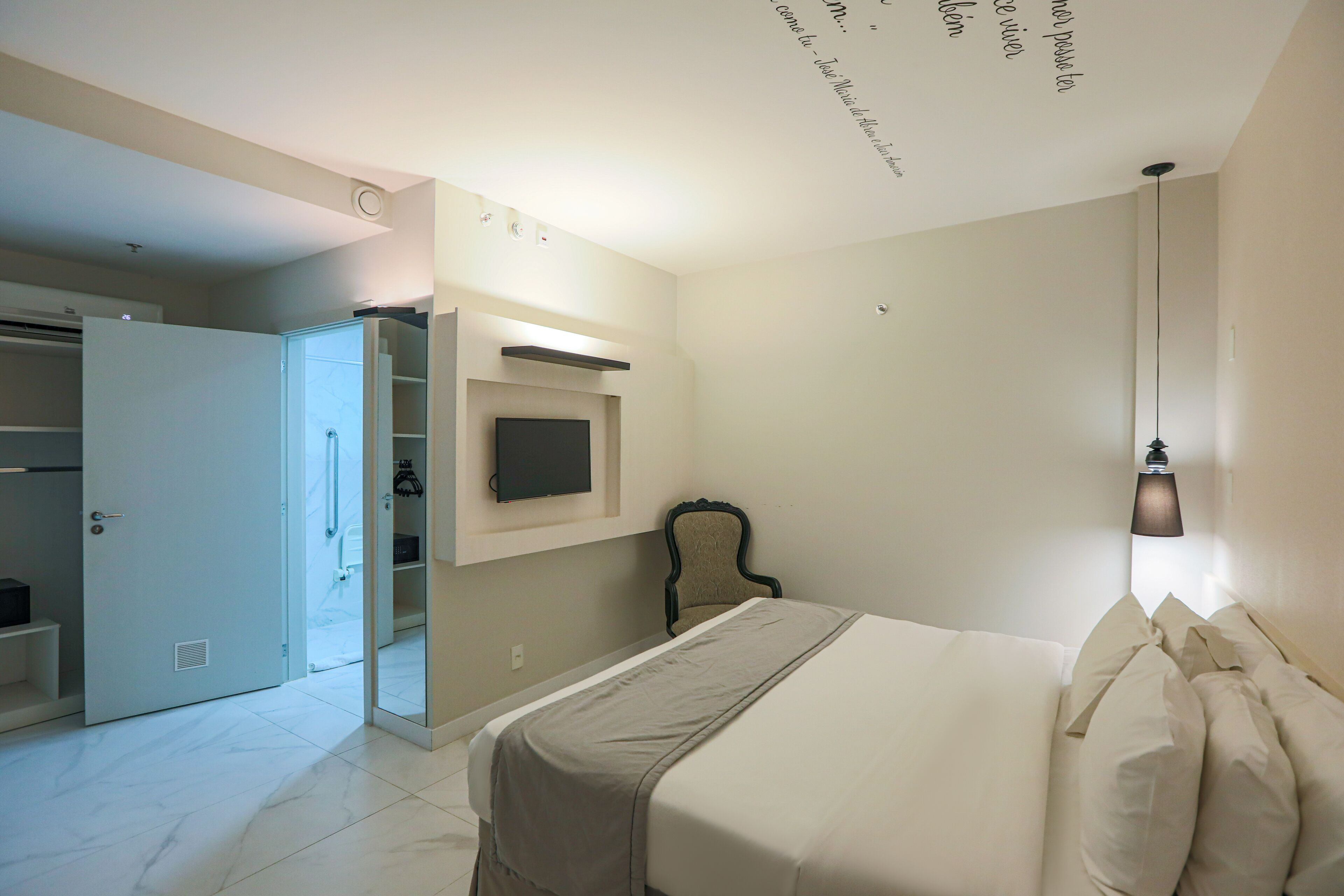 A hotel room with a bed, a television mounted on the wall, a wardrobe, and a ceiling light fixture.