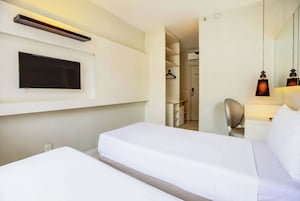 Een hotelkamer met een bed, een aan de muur bevestigde televisie, een spiegel en een nachtkastje met een lamp.