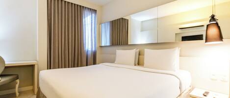 A hotel room with a large bed, a desk, a chair, a mirror, and a hanging light fixture.