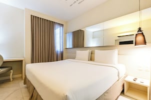 A hotel room with a large bed, a desk, a chair, a mirror, and a hanging light fixture.